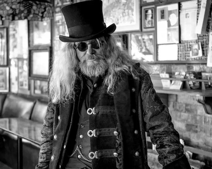 Old rocker with long hair, sunglasses and top hat in a pub, black and white picture