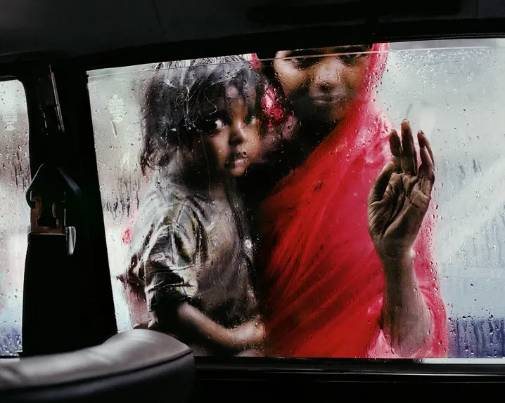 Poor woman with a child in her arms looking into a car from the outside