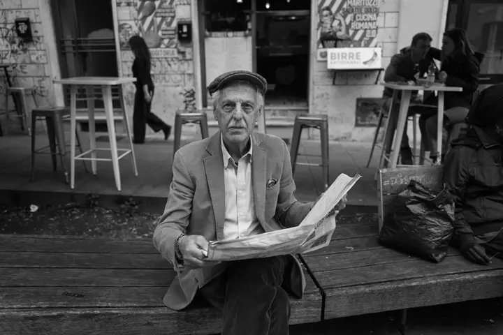 Old man sitting with newspaper on a bench in front of a café, black and white photograph