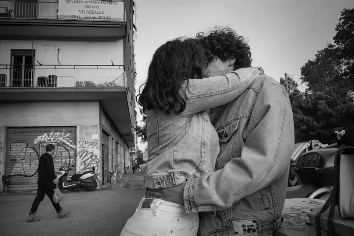 Black and white street photograph of two people kissing in front of an old building