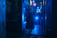 Person walking a dog through a narrow alley at night, illuminated by blue neon lights.
