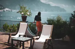 Woman on a large balcony with a view of a lake and mountains.