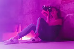 Alex Drewniak sits on the floor, taking pictures in a room lit by pink-purple light.