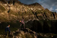 Two children climbing rocks in a mountain landscape at sunset.