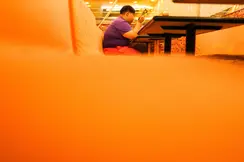 Close-up of an orange bench in a restaurant with a person sitting and eating in the background.