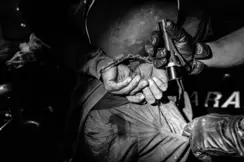 Close-up of a handcuffed person and another person searching his pants pocket with a flashlight.