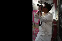 Patrick Domingo takes a photo standing in front of a graffiti wall.