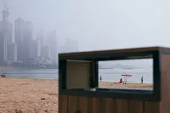 View through the rectangular opening of a garbage can on the beach with skyscrapers in the foggy background.