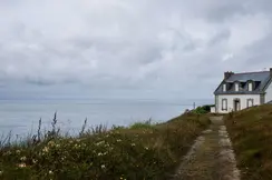 White house on a cliff, surrounded by flowers and a view of the cloudy sea.