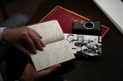 Person holding an old paper notebook, a photograph and a camera lie on the table.