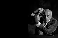 Elderly man holds a camera in front of his face and turns the lens of the camera.