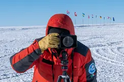 Person takes a photo in a snowy landscape with European flags in the background.