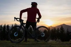 Man leaning on his mountain bike looking at the mountains at sunset.