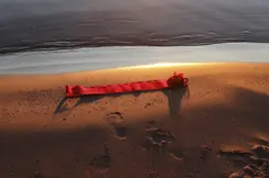 Red ribbon lying on the beach shore at sunset, footprints in the sand.