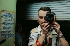 Philipp Reinhard looks through a camera and stands in front of a blue garage door.