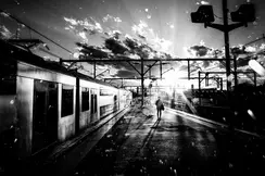 A person stands on a platform next to a train while the sun casts shadows.