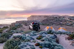 A jeep and two tents on a coast at sunset.
