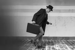 Elderly man in suit with hat and briefcase walking on icy cobblestones.