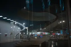 Reflection of a spiral staircase and a city at night in the glass front of a building.