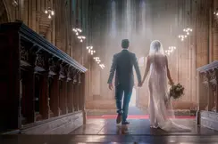 A bride and groom walk hand in hand down the aisle of an impressive church.