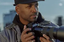 Close-up of a man holding a camera with skyscrapers in the background. 