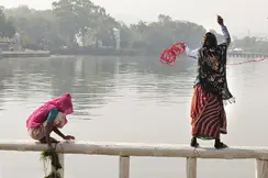 A woman and a child are standing on a railing in front of a lake and are fishing.
