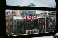 View from a window of a city with a building bearing the graffiti ‘LOVE ME’.