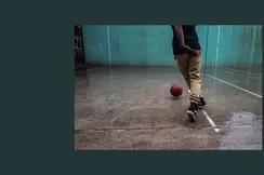 Person playing basketball on a wet court with a turquoise wall in the background.
