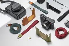 Leica camera with various straps, protective covers and accessories on a light background.