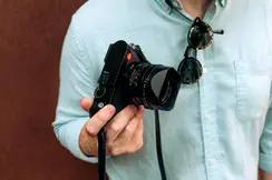 A man wearing a blue shirt holding a Leica camera in his right hand