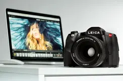 Leica camera on a table in front of a laptop showing a portrait photo.