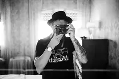 A person stands in a room and looks through a camera to take a photo.