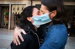 A couple wearing face masks hug and kiss in a street