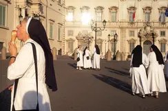 A nun eats an ice cream while several nuns talk in the background.