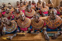 Women from the Samburu tribe in Kenya sitting on a wooden bench in traditional clothes and smiling.