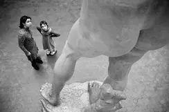 Two people stand in front of a large statue and look upwards.