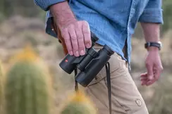 The Leica Trinovid is held in one hand by a man. He carries it casually beside him as he wanders through the landscape