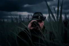A hunter standing among tall grass at dusk with the Leica Calonox 2 in focus