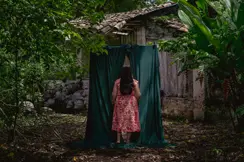 Woman in the forest walks through a green curtain behind a forest house