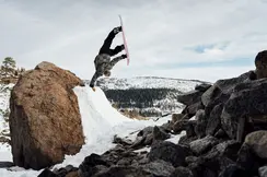 Snowboarder does a one-armed handstand on a ramp in the mountains