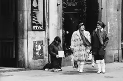 Two smartly dressed women walk past a homeless person.