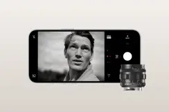 An iPhone displays an image with a man. In front of the phone is a Leica lense.