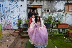 Young woman in a formal quinceañera dress surrounded by family, capturing a milestone celebration within a modest residential setting.