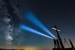 Two people shining headlamps beneath a star-filled night sky and the Milky Way.