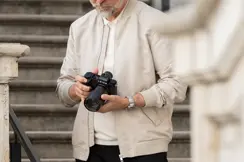Photographer adjusting a Leica camera near an urban staircase.
