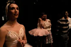 Ballet dancers embracing backstage after a performance while others wait in the wings.