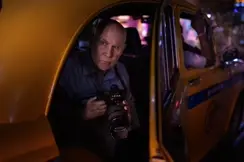Photographer holding a Leica SL camera while seated inside a yellow taxi at night, illuminated by colorful urban lights.