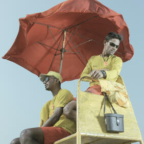 two men sitting under red umbrella