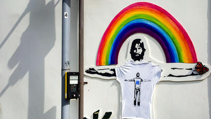 A mural on the wall of a man with outstretched arms in front of a rainbow.