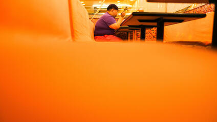 Close-up of an orange bench in a restaurant with a person sitting and eating in the background.